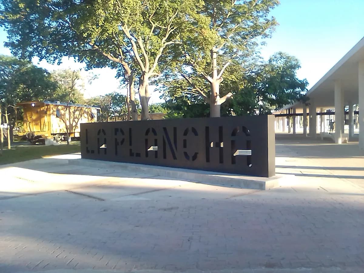 Letrero de acero con la palabra La Plancha en una plaza del parque, bajo los árboles